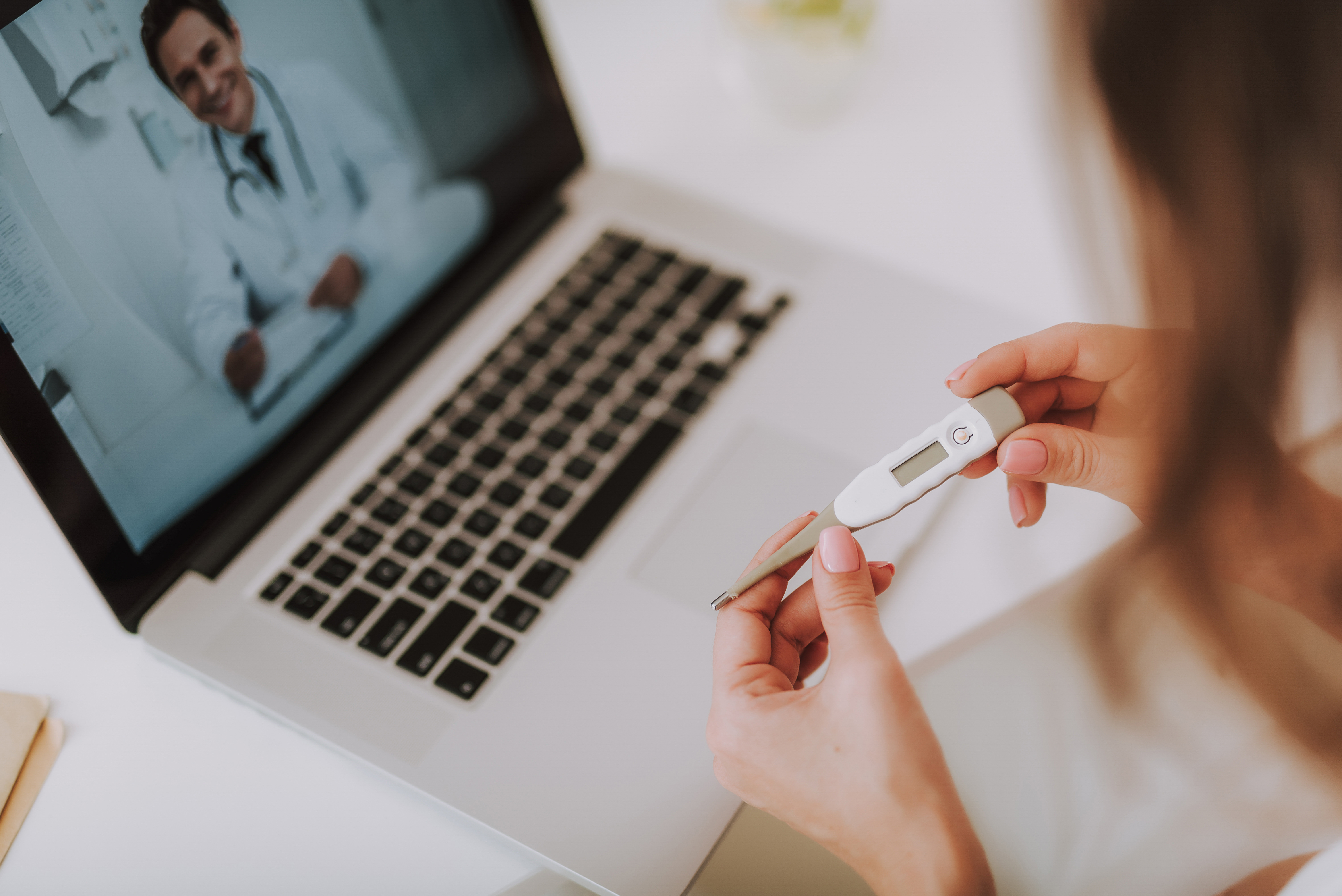 Cropped close up photo of pregnancy test. Lady looking at test and sitting talking with smart doctor while using pc laptop